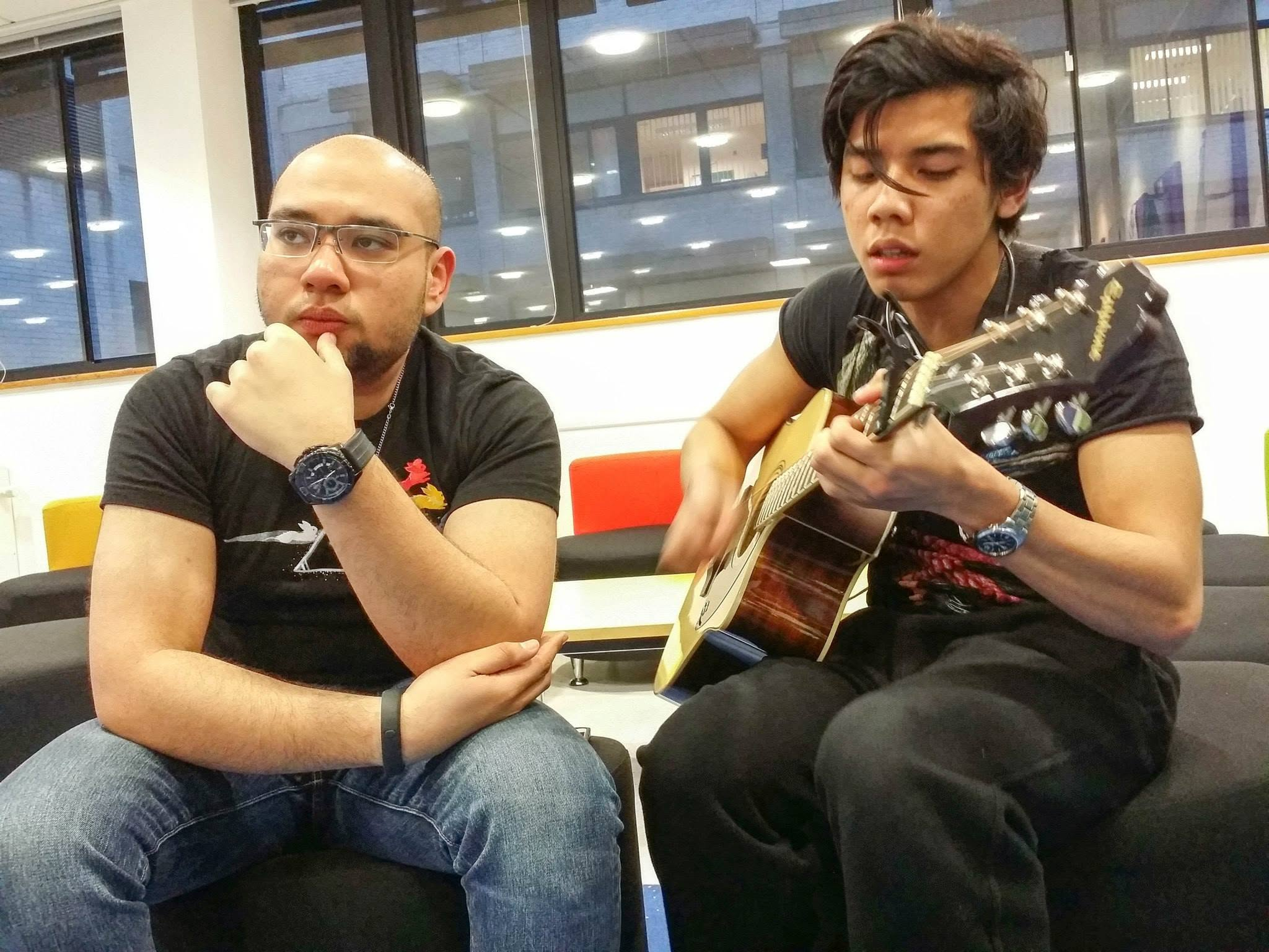 Hykarl Sufardi, seated on the left with his hand beneath his chin, beside a person playing an acoustic guitar.