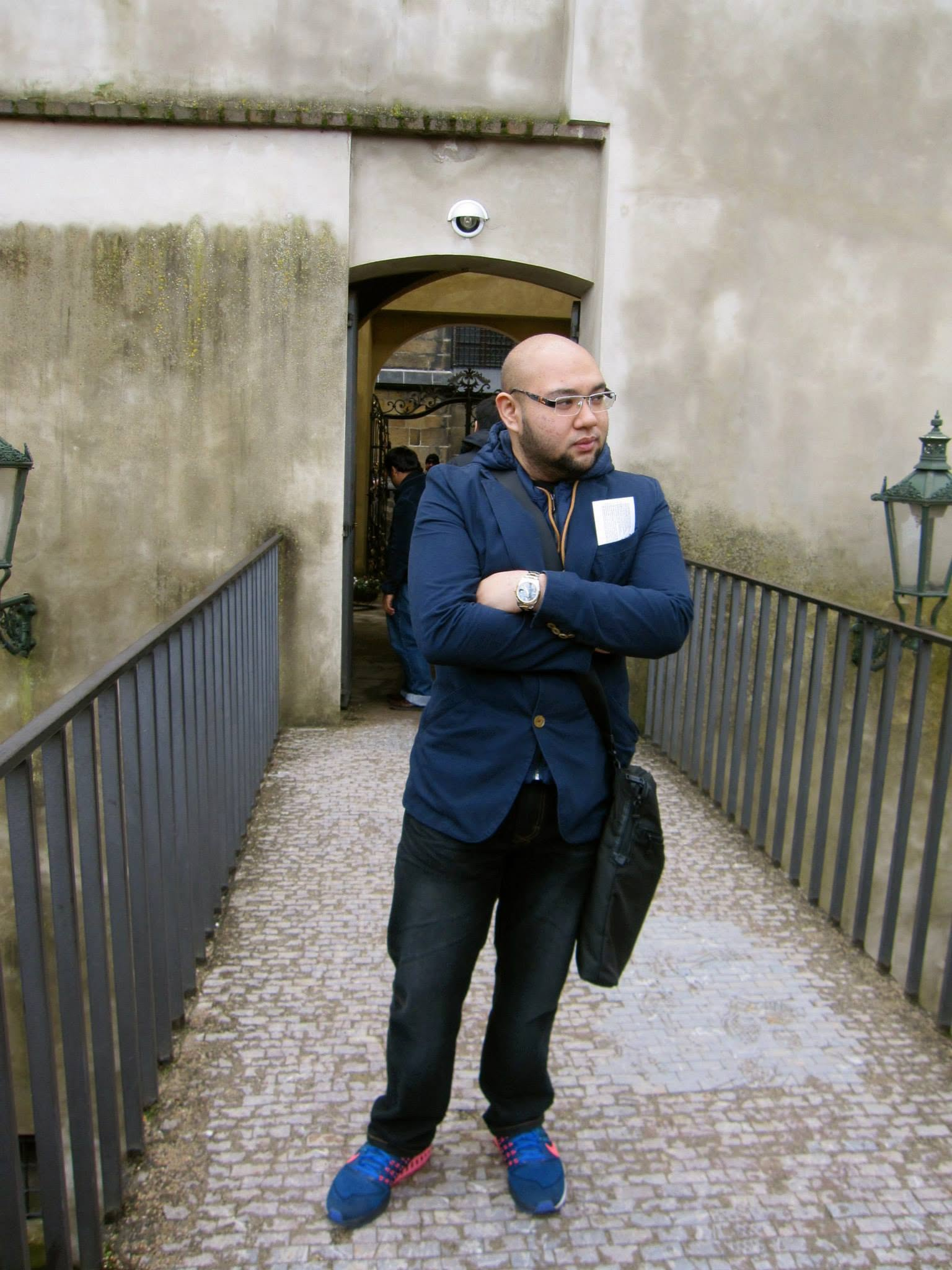 Hykarl Sufardi in glasses and a navy jacket, standing with folded arms on a cobbled walkway.